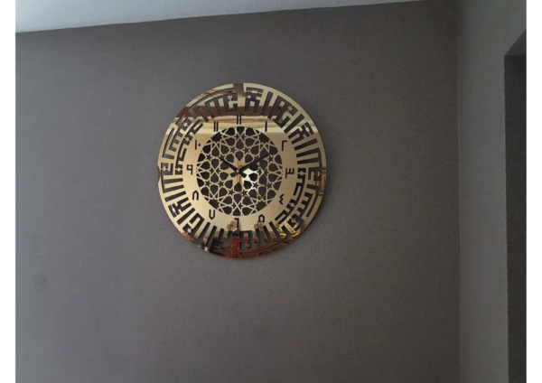 a golden color clock with the first kalima on the wall